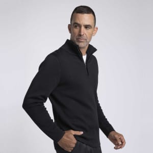 A man wearing a black zippered sweater, standing in profile against a neutral background. The sweater has a sleek, modern design.