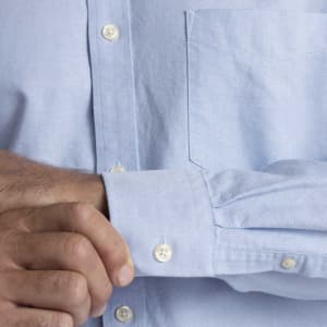 Light blue button-up shirt with a chest pocket and cuff detailing, featuring a logo on the chest.