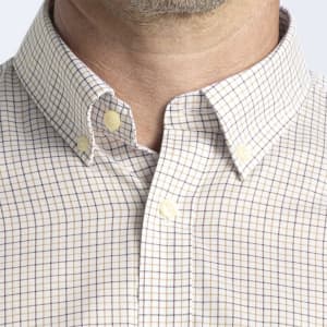 A button-up shirt featuring a check pattern in beige and navy, with a button-down collar. It has a logo on the chest.