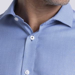 A close-up of a men's button-up shirt featuring a blue checkered pattern and white buttons. The shirt has a logo.