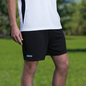 A pair of black sports shorts with a logo, featured against a green outdoor background.