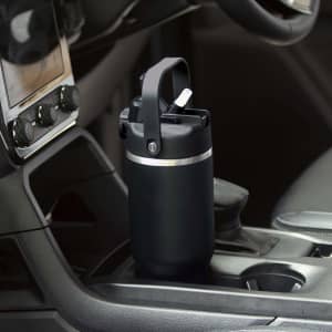 A drink bottle with a black exterior and a handle, placed in a vehicle's cup holder. It has a sleek design and a logo.