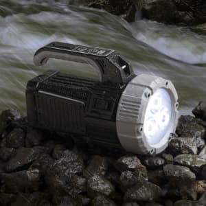 A black and silver torch rests on rocky ground, with a bright light emitting from its front, surrounded by flowing water.