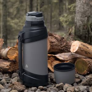 A drink bottle with a grey and black exterior, accompanied by a removable cup, set against a natural backdrop.