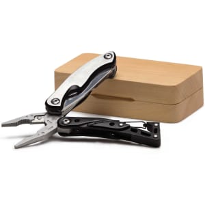 A multi-tool with pliers features a silver and black design, displayed beside a wooden box.