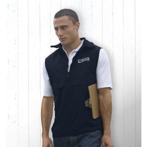 A man in a black nylon vest with a logo, holding a clipboard against a white wooden background.