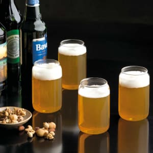 Four clear beer glasses filled with pale golden beer and topped with frothy white foam, set against a dark background.