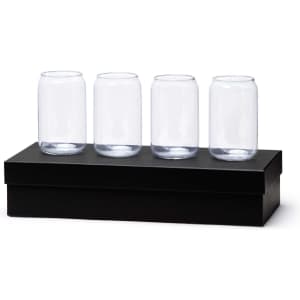 A set of four clear glass beer cans displayed on a black box. The glasses are identical in shape and size.