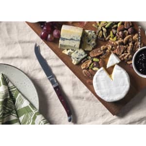 A cheese knife with a wooden handle on a cheese board featuring a variety of cheeses, nuts, and fruits.
