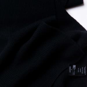 A black 100% Merino scarf, featuring a soft ribbed texture and a label.