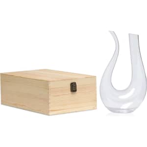 A clear glass wine decanter with a unique shape beside a wooden box.