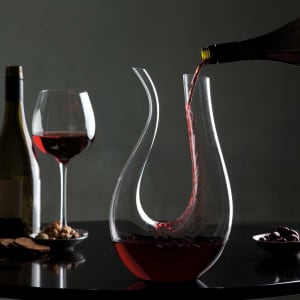 A glass Barolo wine decanter pouring red wine, with a wine bottle and glass in the background. Elegant design.