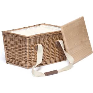 A wicker picnic basket in natural tones with a wooden lid and cream lining, featuring sturdy fabric handles.