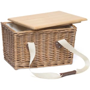 A wicker picnic basket with a wooden lid and a cream-coloured strap for carrying. It has a branded logo.