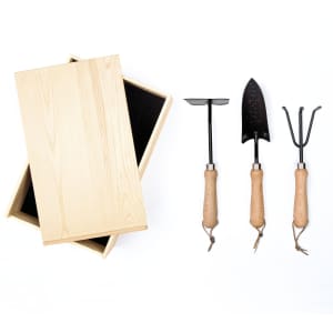 A wooden box with a black interior, alongside three garden tools with wooden handles: a trowel, cultivator, and hand rake.