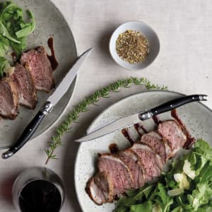 A knife set with sleek black handles, featured alongside sliced meat on rustic plates with salad and herbs.