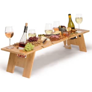A wooden tabletop in natural colour, featuring wine bottles, glasses, and an array of fruits and cheeses.
