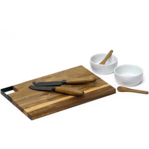 A wooden cheese board with two cheese knives, two white bowls, and a small wooden spoon.