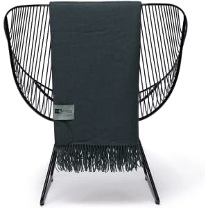 A dark green Merino wool blanket with fringed edges, displayed on a modern wire chair, featuring a branding label.