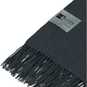 A dark grey merino blanket with a textured pattern and fringed edges, featuring a small branding label.