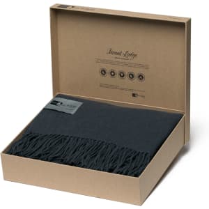 A dark grey Merino blanket with a fringed edge, presented in a stylish brown box with branding.
