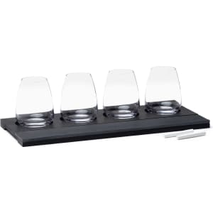 A wine tasting set featuring four clear glasses on a black wooden tray, accompanied by two white chalk sticks.