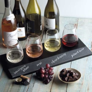 A wine tasting set featuring four glasses of different wines, a slate tray with inscriptions, and dark chocolate pieces.