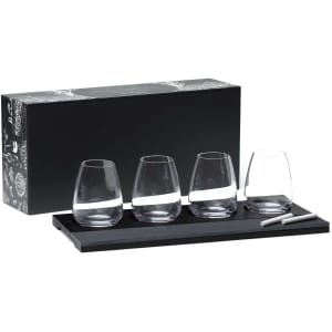 A set of four clear wine glasses on a black tray, accompanied by a chalk marker, all packaged in a decorative box.
