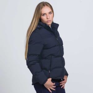 A woman wearing a navy blue puffer jacket, featuring a zip front and a high collar, with a logo visible.