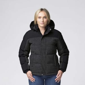 A woman wearing a black and grey smpli XT Plunge Jacket with a hood, featuring a logo on the left chest.
