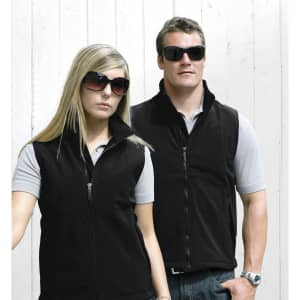 A black soft shell vest is worn by a man and a woman, both in sunglasses, against a light wooden background.