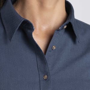 A close-up of a women's button-up shirt in dark blue, featuring a collar and button details. It has a logo.