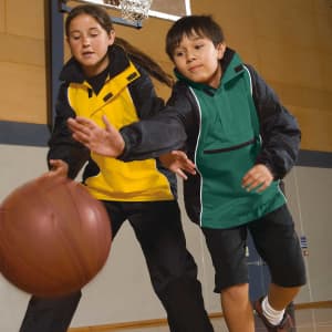 A yellow and green rain jacket worn by two children playing basketball indoors. Both jackets have logos.