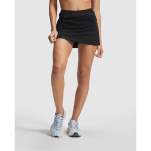 A black tennis skort featuring an elastic waist, paired with light blue sports shoes. The skort has a simple design and a logo.