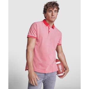 A young man holds a football while wearing a pink polo shirt with red accents and a collar.