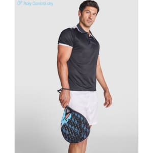 A man in a black polo shirt with white accents holds a sports racket, wearing white shorts. The shirt features a logo.