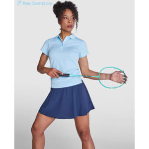 A woman models a light blue polo shirt and a navy skirt, holding a racket. The shirt features a logo.