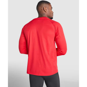 A long-sleeved t-shirt in red, shown from the back on a model wearing black pants. The shirt features a branded logo.