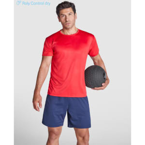 A red t-shirt featuring a logo, worn by a man holding a black exercise ball, paired with navy shorts.