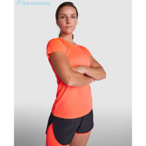 An orange women's T-shirt with a fitted design, paired with black athletic shorts. The model stands confidently.