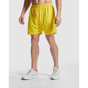 Yellow sports shorts with an elastic waistband, worn by a model alongside white athletic shoes.