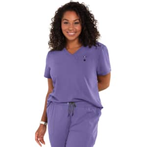 A woman wearing a purple medical scrub top with a pocket and a logo, smiling against a white background.