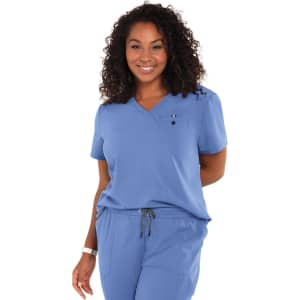 A woman wearing a short-sleeved, blue top with a pocket, part of a scrub set, smiling at the camera.