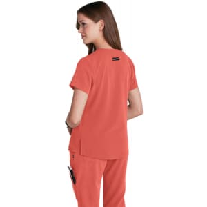 A back view of a woman wearing a coral-coloured top with a logo on the upper back. The top features short sleeves.