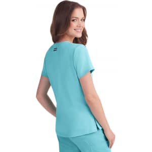 A woman in a turquoise short-sleeved top smiling over her shoulder, featuring a small logo on the back.
