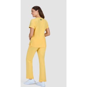 A woman wearing a yellow top and matching pants, standing with her back to the camera. The outfit has a logo on the back.