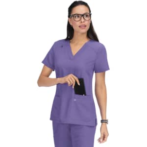 A purple scrub top with a V-neck and two front pockets, featuring a branding logo on the sleeve.