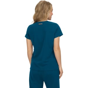 A back view of a teal top with short sleeves, featuring a logo. The model has wavy blonde hair.