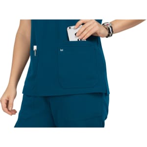 A teal top featuring a pocket with a phone partially visible, alongside a pen holder, and a logo on the pocket.