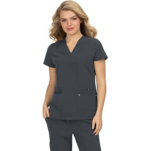 A woman wearing a grey scrub top with a v-neck and two front pockets, featuring a logo on one pocket.